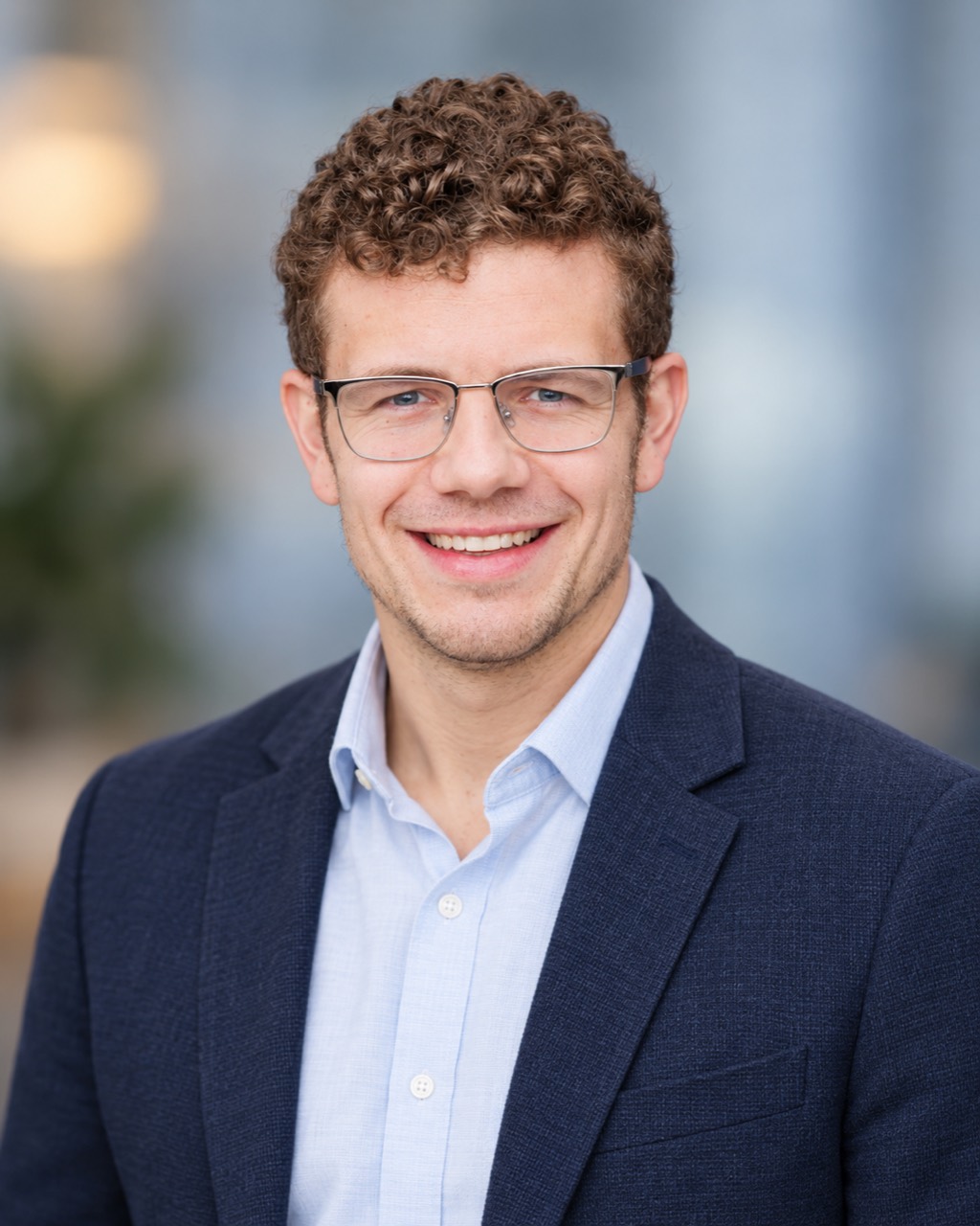 Graham Grome smiling, wearing glasses and a navy blazer.
